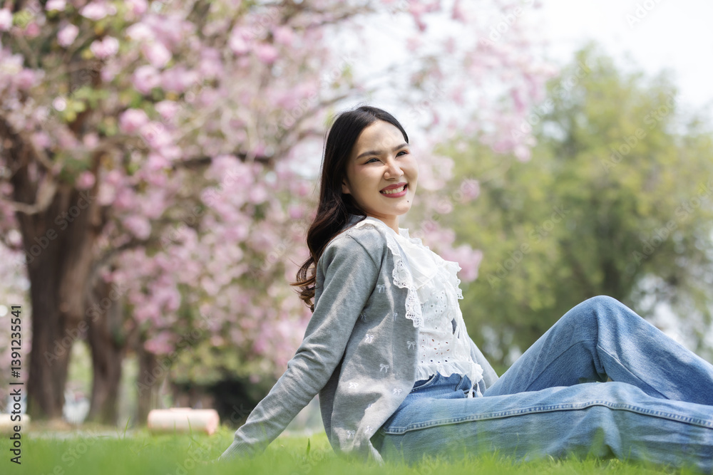 A cheerful young woman sits on the grass under blooming pink trees, enjoying a bright spring day. Dressed in a lace blouse and casual jeans, she radiates happiness and tranquility in nature. A cheerful young woman sits on the grass under blooming pink trees, enjoying a bright spring day. Dressed in a lace blouse and casual jeans, she radiates happiness and tranquility in nature.