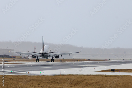 Aircraft landing on runway under overcast skies during inclement weather conditions at an airport