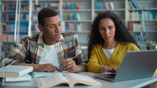 Classmates students African American man Arabian Latina woman together work high school library study homework team project writing information laptop computer dictate girl guy diploma university tech