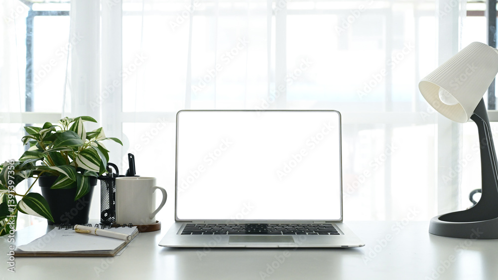A laptop sits on a desk with a plant and a cup. The laptop is open and the screen is blank. A laptop sits on a desk with a plant and a cup. The laptop is open and the screen is blank.