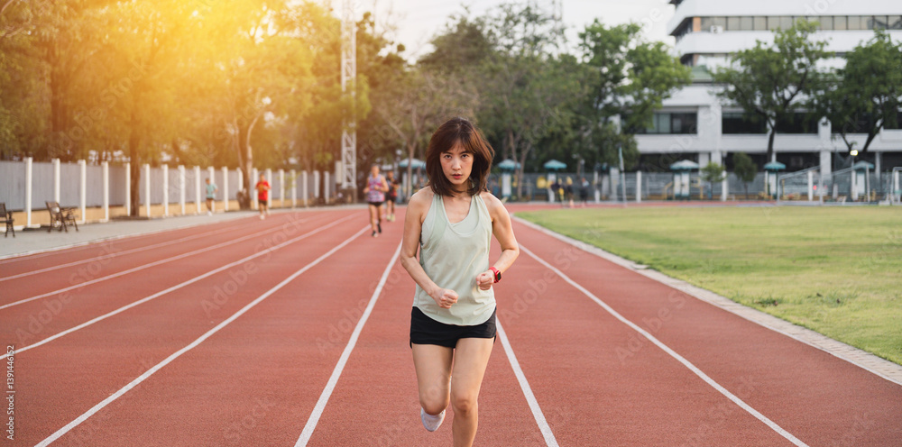 Obraz premium focused southeast Asian woman runner is jogging on red track in outdoor stadium during sunset, embracing healthy lifestyle and wellness with motivation and challenge