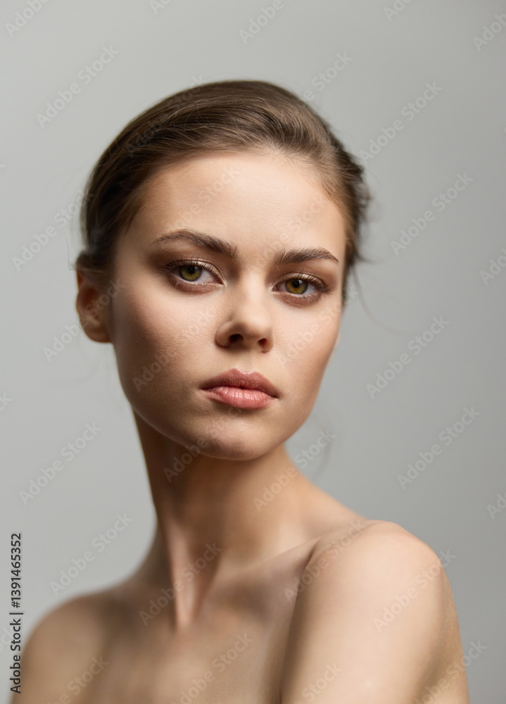 Beautiful young woman with natural makeup, posing against a soft gray background, exuding confidence and calmness. Portrait focusing on beauty and elegance.