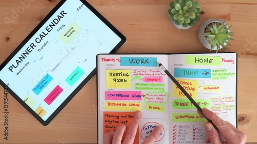 Top view of a manager organizing work and personal appointments, writing on a notebook and checking a digital calendar on a tablet, creating a productive schedule