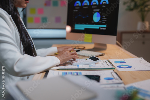 Businesswoman using calculator and working with financial charts and graphs showing company growth and analyzing marketing research data at night in office