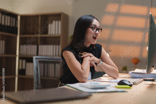Excited businesswoman is celebrating a success while working at her desk in an office at night, looking at her computer screen with a joyful expression