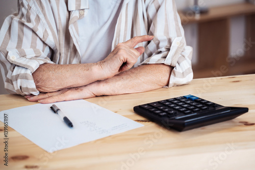 elderly woman sitting at home at the desk with calculator and calculating finances or taxes. Senior retired woman counting income and profit. Pension calculation concept