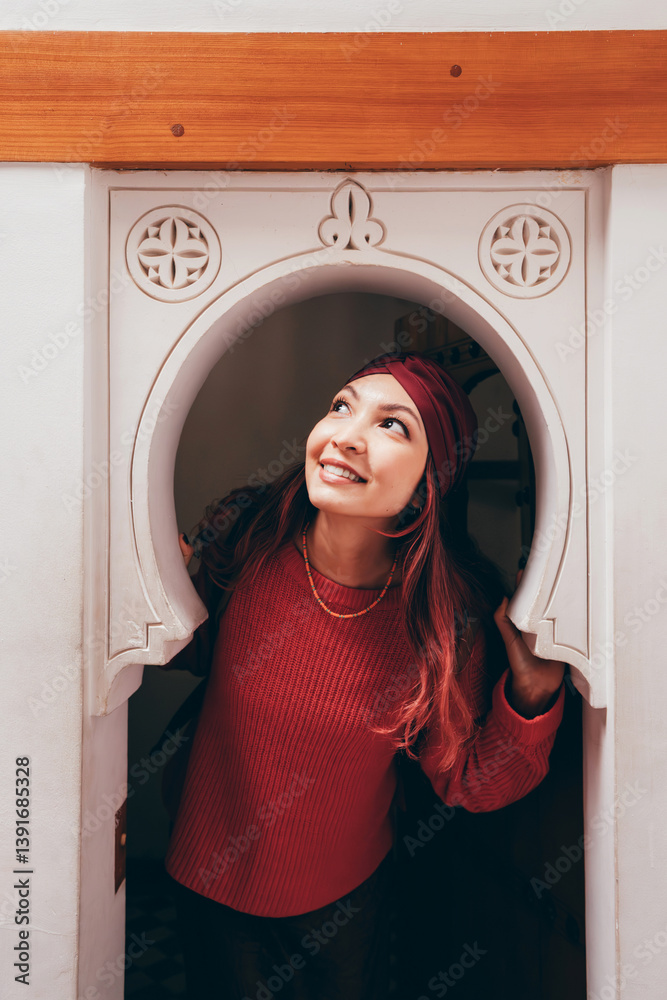 Young woman with a headscarf looking up and smiling while exploring traditional Moroccan architecture