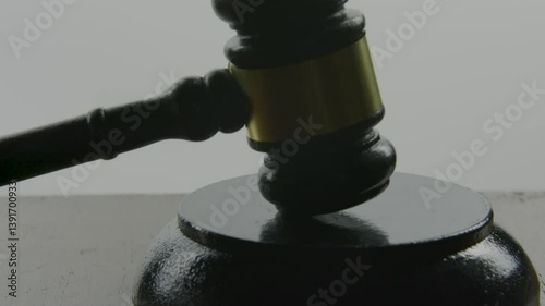 A close-up silhouette of a gavel being lifted and struck once, followed by three times, against a stark white background, symbolizing justice, authority, and the finality of a decision