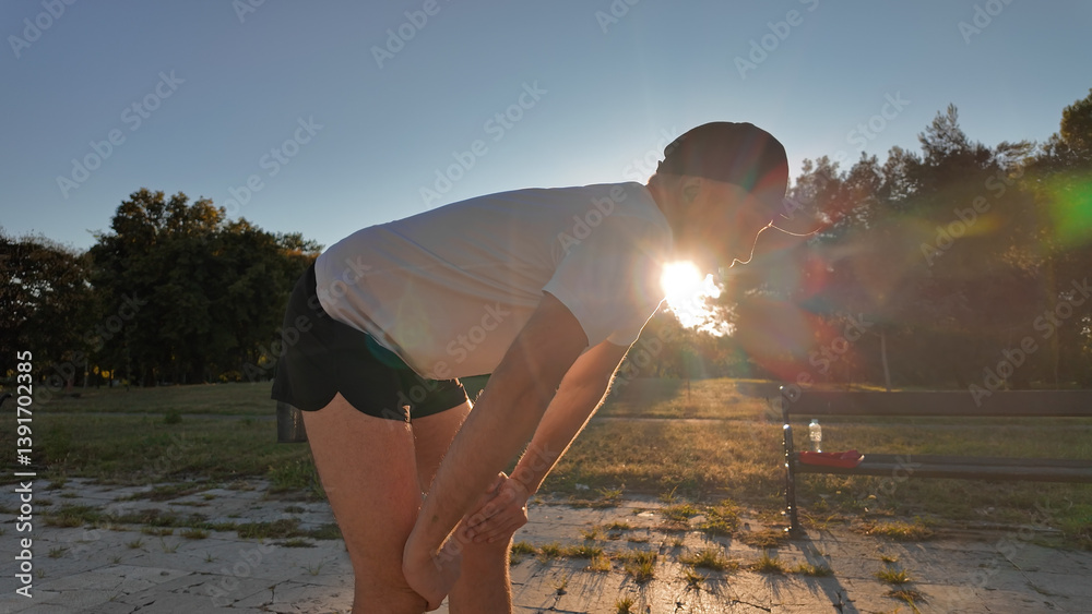 Man taking a break after exercising and jogging in an urban park during sunset hours.
