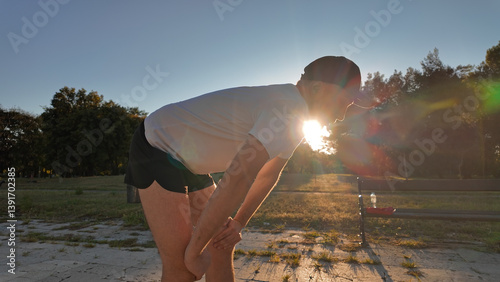 Obraz na płótnie Man taking a break after exercising and jogging in an urban park during sunset hours. w salonie
