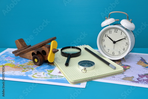A still life about time to travel on the blue  wooden background  with retro alarm clock, wooden retro model of airplane, world maps, compass, magnifier, notebook and pencil. Concept of travel. 