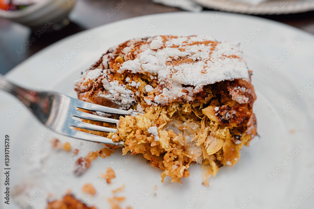 Close up of a fork picking a piece of delicious chicken pastilla, a traditional Moroccan dish, sprinkled with powdered sugar and cinnamon