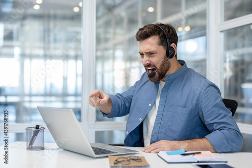 Obraz na płótnie A furious customer service representative, wearing a headset, has an outburst in response to a problem on his laptop. He points and shouts with a displeased expression. w salonie