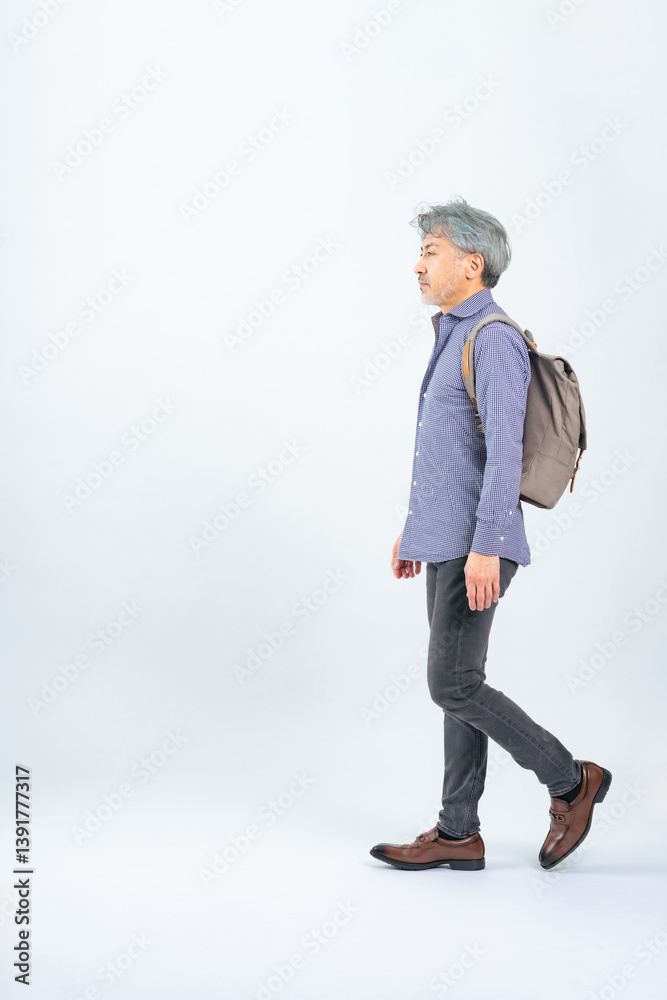 リュックを背負って横向きに歩くシニア男性の全身写真
