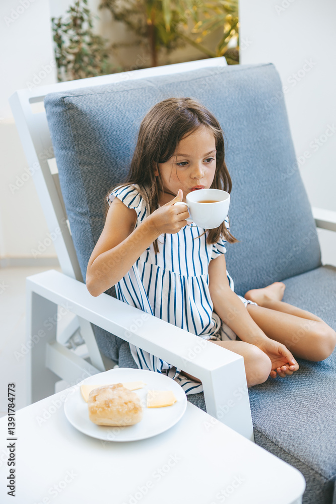 Young girl sitting comfortably on a chair, sipping tea with a calm expression Young girl sitting comfortably on a chair, sipping tea with a calm expression