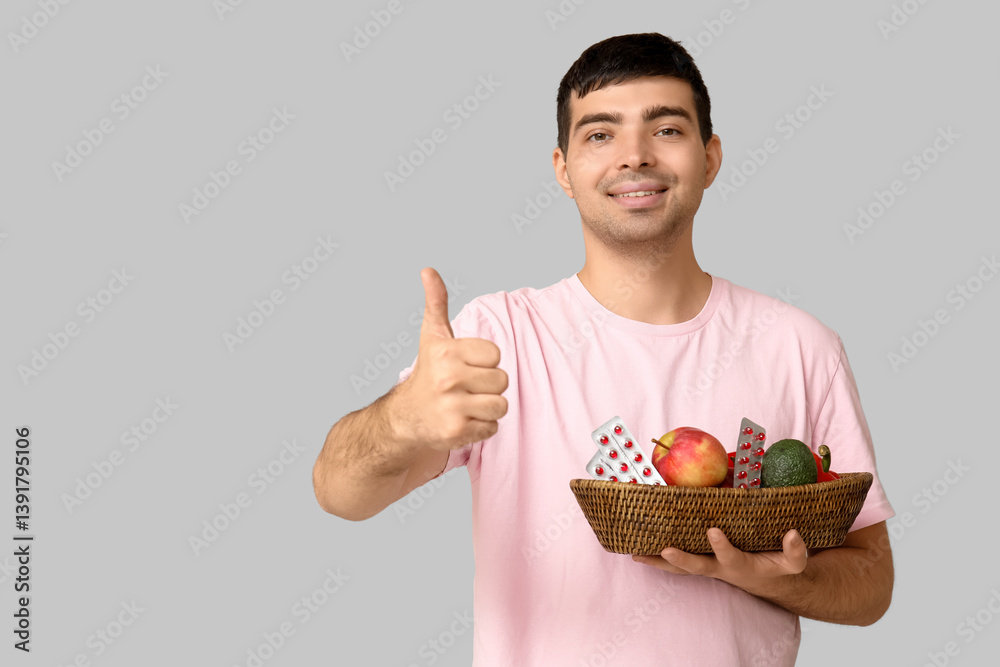Young man with vitamin A pills and healthy food showing thumb-up on light background Young man with vitamin A pills and healthy food showing thumb-up on light background