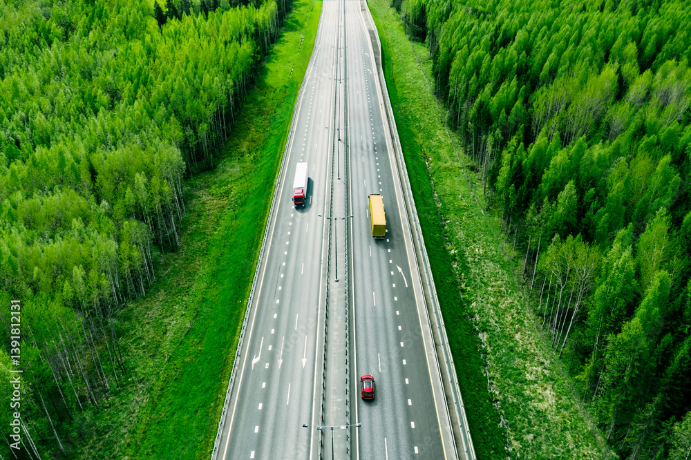 Aerial view of highway with red car and modern semi trailers trucks, green trees and summer forests around