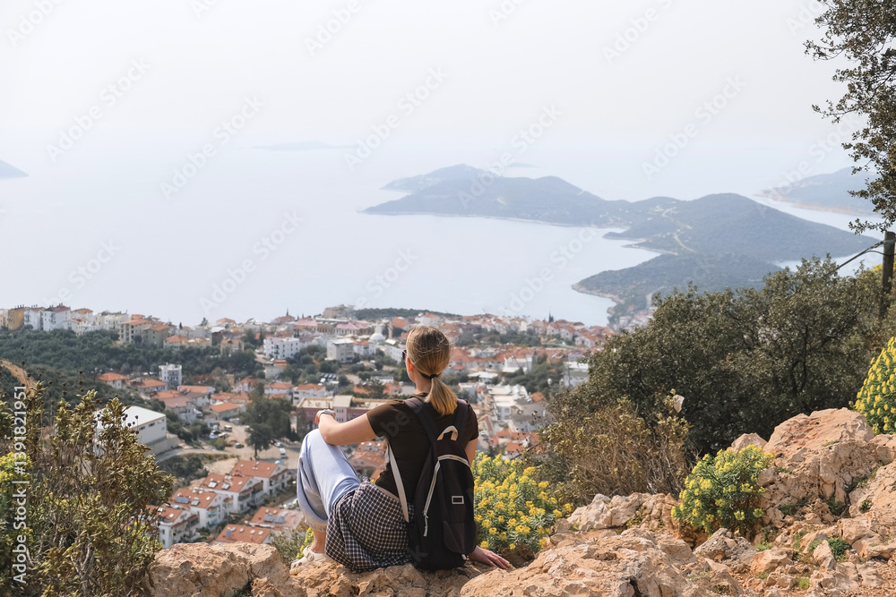 Fototapeta premium Solo female traveler sitting cliff overlooking Mediterranean coast.Eco travel,hiking, digital nomad lifestyle,nature,adventure,road trip,travel influencer freedom, scenic view, summer exploration..
