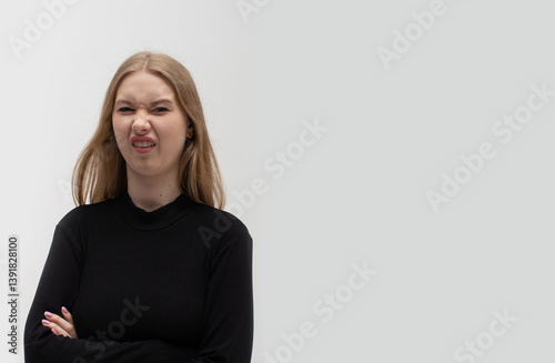 A young blonde girl wearing casual dark clothes has a disgusted expression, displeased and fearful, making a disgusted face because of aversion reaction. Close-up portrait.
