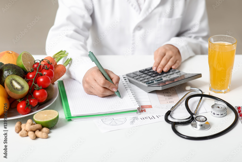 Young female nutritionist with healthy food, glass of juice and calculator writing diet plan in office, closeup