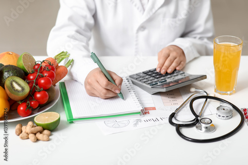 Obraz na płótnie Young female nutritionist with healthy food, glass of juice and calculator writing diet plan in office, closeup w salonie