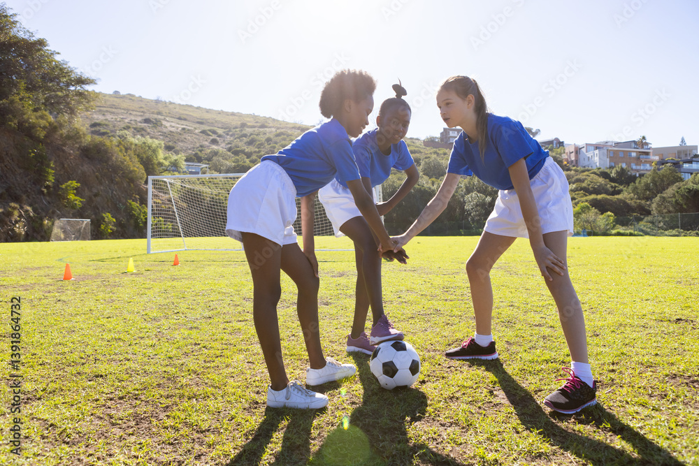 Playing soccer, three school diverse girls in sports uniforms strategizing on field
