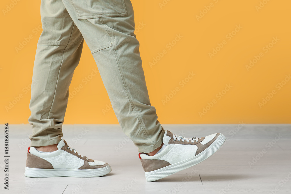 Young man in stylish sneakers near yellow wall, closeup