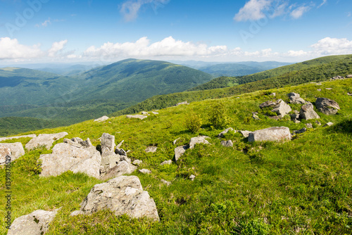 Obraz na płótnie green alpine hills and slopes in summer. landscape with stones and boulders among the grass under a blue sky with clouds. view in to valley scenic vacations in mountains of ukraine on a sunny morning w salonie
