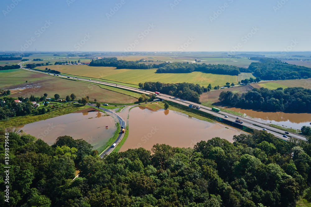 Aerial view of flooded fields and submerged rural road near busy highway. Concept of climate impact, transportation disruption and natural disaster