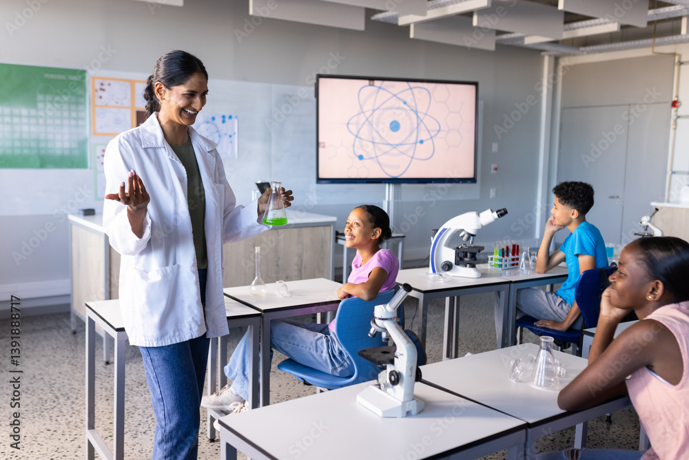 Fototapeta premium In school, Indian female teacher conducting science experiment with students in classroom