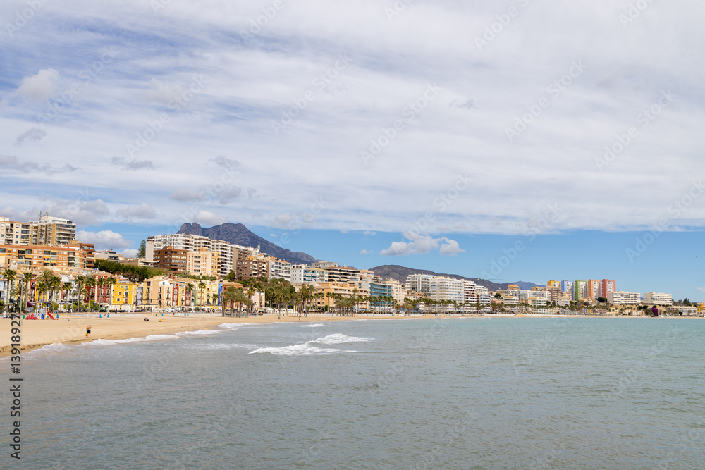 Photo of the beautiful town of Villajoyosa in Spain showing the beach front on a sunny day with hotels and guest houses on the beach front showing the sandy beach and ocean front