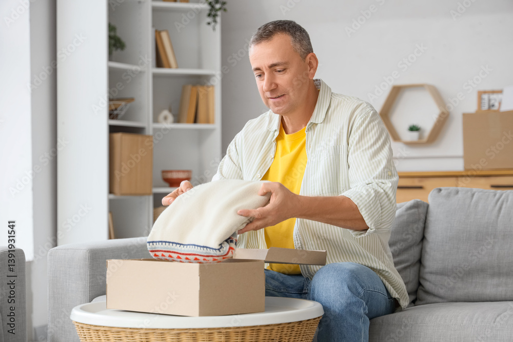 Mature man unpacking box with sweater at home