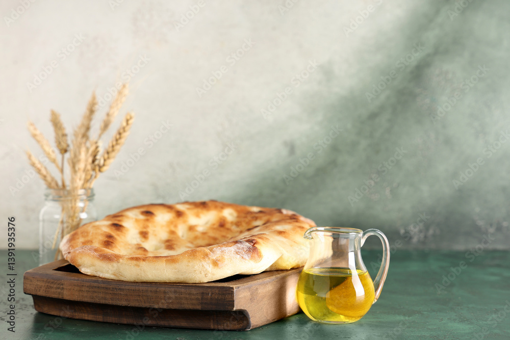 Wooden tray with tasty lavash and jug of oil on green grunge table