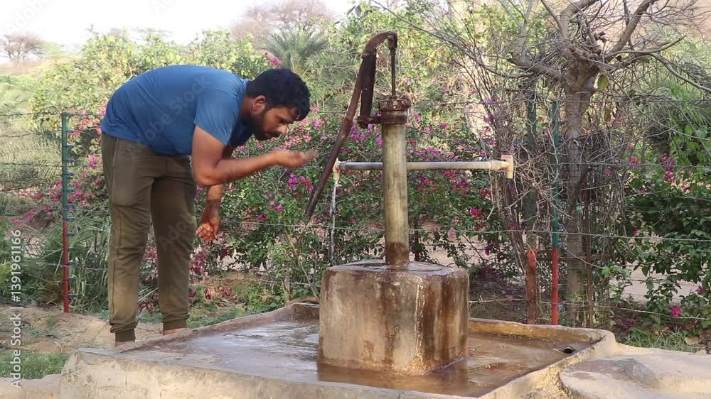 A man drinking water directly from a hand pump in a rural area, depicting traditional lifestyle and access to groundwater in Indian villages