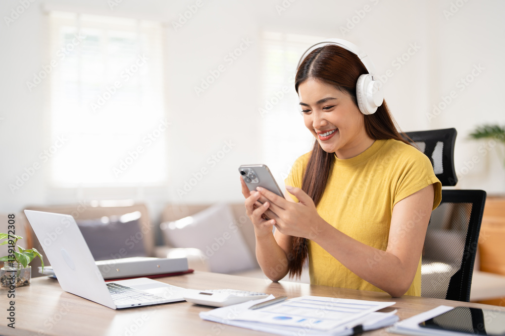 Business woman with laptop using mobile phone and listening music through headphones at home office. Business woman with laptop using mobile phone and listening music through headphones at home office.