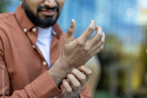 A man scratches his wrist, possibly due to itching or discomfort. The focus is on his hands and part of his face.