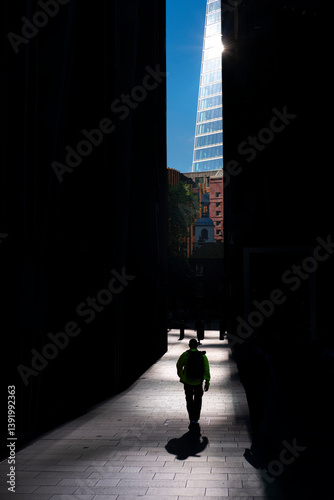 Silhouetted figure walking toward sunlight between towers, symbolizing clarity, decision and leadership in business.