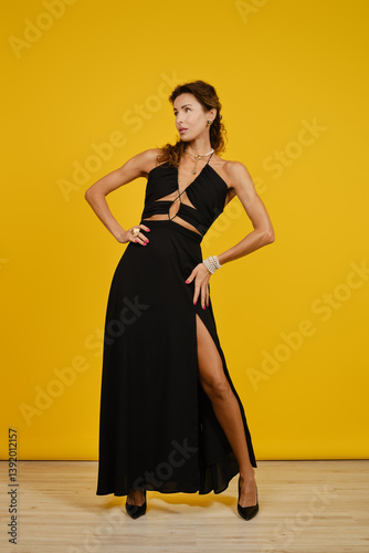 Fashion model showcases elegant black high-slit dress dress against bright yellow background