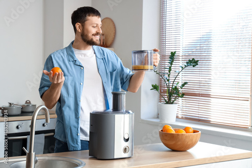 Young man with fresh orange juice and modern juicer in kitchen