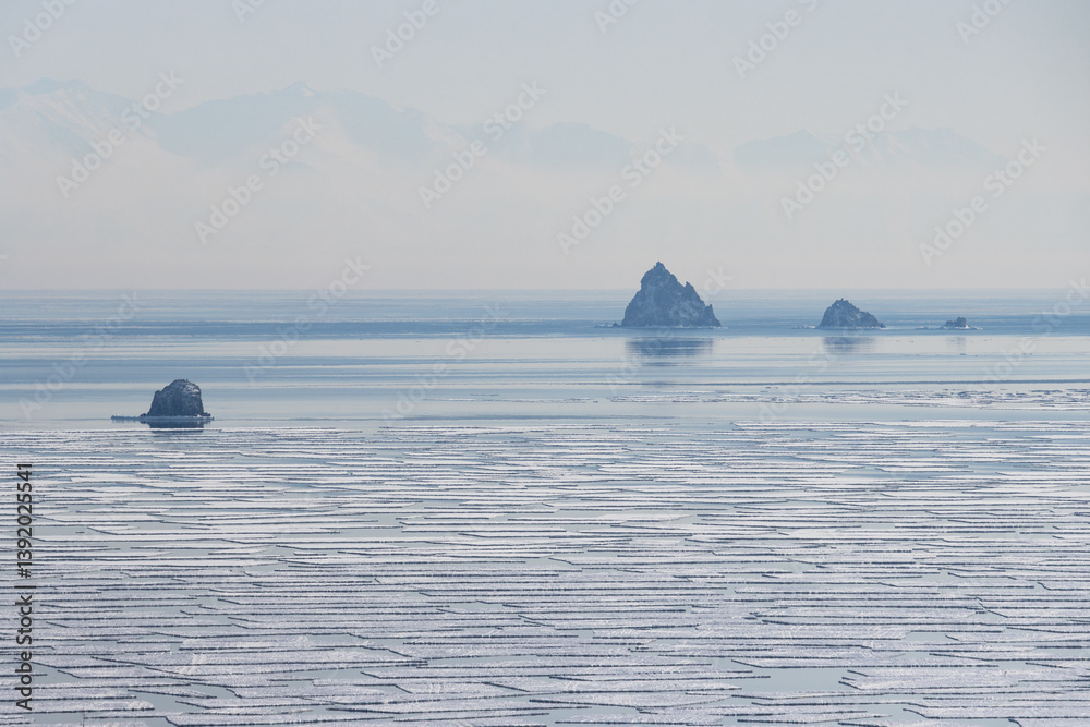 View of small rocky islands in the sea. In the foreground are many ice floes. In the distance, mountains in the haze. Sea of Okhotsk, Magadan Region, Russia. Kekurny and Three Brothers Islands.
