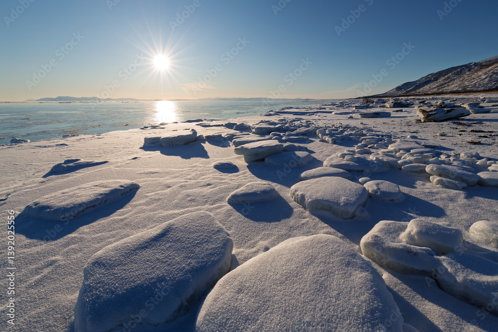 Winter seascape. View of ice floes on the seashore. Snow-covered ice. In the distance, unfrozen sea. Bright sunlight. Cold weather. Coast of the Sea of Okhotsk, Magadan region, Far East of Russia.