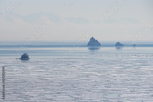 Obraz na płótnie View of small rocky islands in the sea. In the foreground are many ice floes. In the distance, mountains in the haze. Sea of Okhotsk, Magadan Region, Russia. Kekurny and Three Brothers Islands. w salonie
