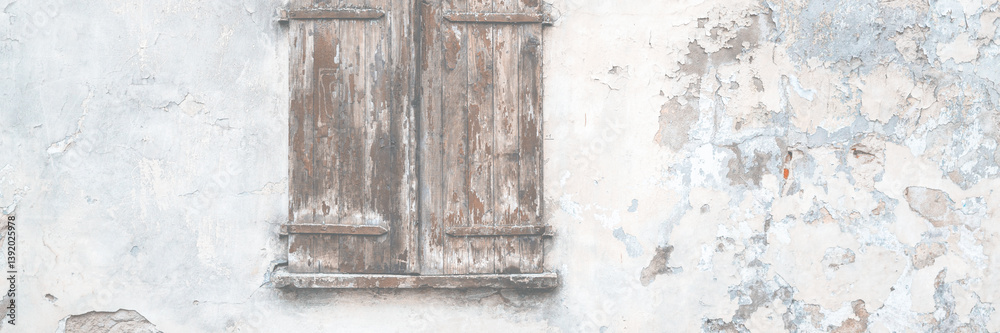 Old wall with peeling plaster. Window covered with wooden shutters. Weathered rough surface of the wall. Medieval European city. Vintage texture for background and design.