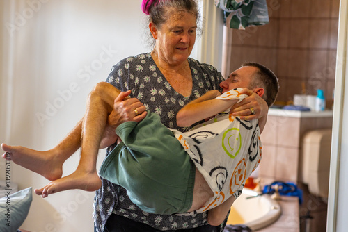 lady carrying her adult son who has cerebral palsy in the house with bathroom through door