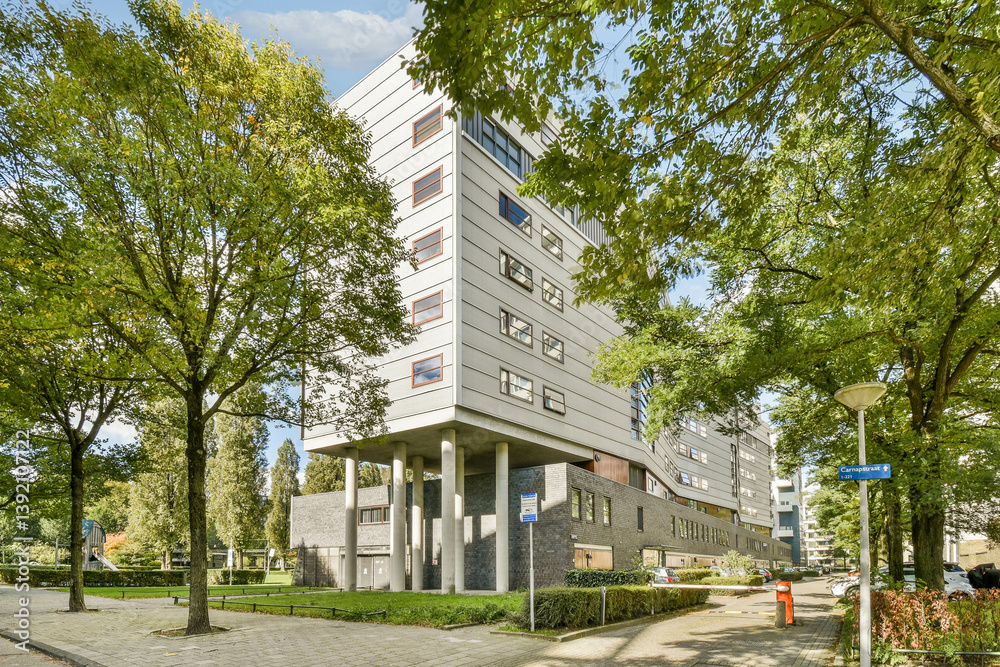 Fototapeta premium A contemporary building featuring modern architecture, nestled among lush trees and a well-maintained landscape in an urban setting.