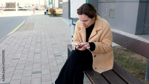 Woman sitting on a bench using her smartphone in a modern urban setting on a sunny day