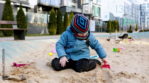 Child playing in sand at urban park during winter, engaging with toys and enjoying outdoor activities in cold weather