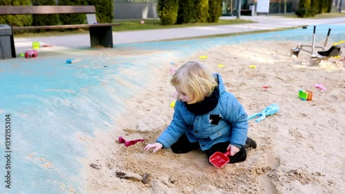 Child enjoys playing in the sand at a park playground on a sunny day