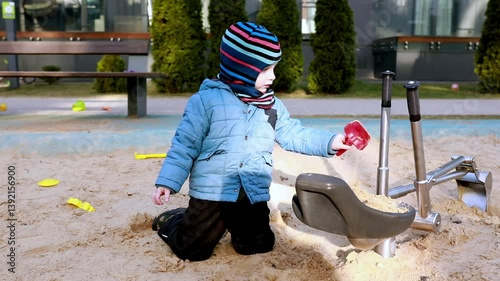 Young child enjoys playing in the sand at a playground during a sunny day in early spring