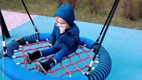 Child enjoys swinging on a colorful net swing at a playground in winter attire during a sunny afternoon